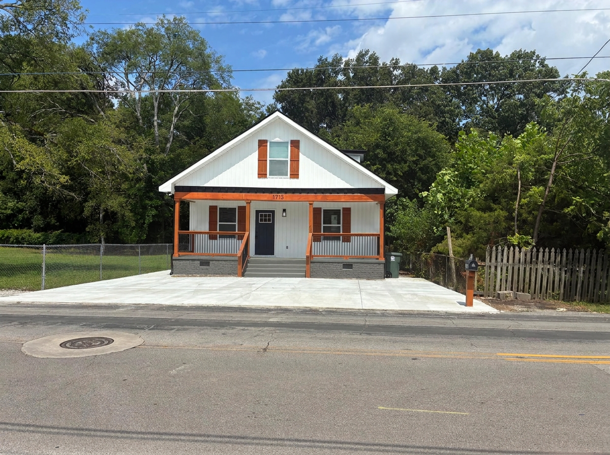 Completed exterior renovation with white siding, cedar porch details, and a new concrete driveway